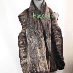 May include: A brown and tan scarf with a textured, felted appearance is draped over a mannequin. The scarf has a marbled effect with darker brown edges and lighter tan and grey tones throughout. The words "Back side" are visible on the scarf.