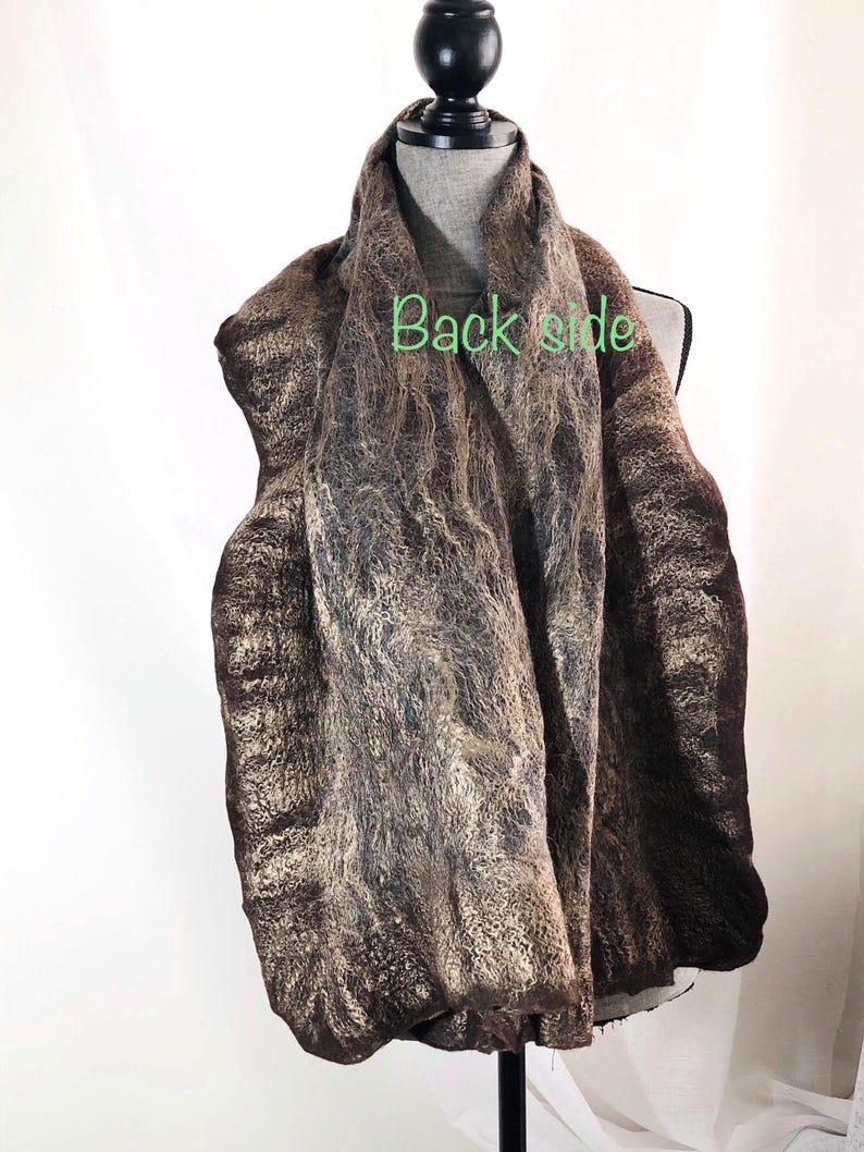 May include: A brown and tan scarf with a textured, felted appearance is draped over a mannequin. The scarf has a marbled effect with darker brown edges and lighter tan and grey tones throughout. The words "Back side" are visible on the scarf.