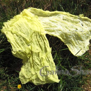 May include: A yellow silk scarf with a crinkled texture. The scarf is draped over green grass.