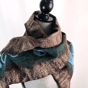 May include: A brown, green, and blue felted wool scarf draped over a mannequin. The scarf features a textured, patterned design with shades of brown, green, and blue. The scarf is made of wool.