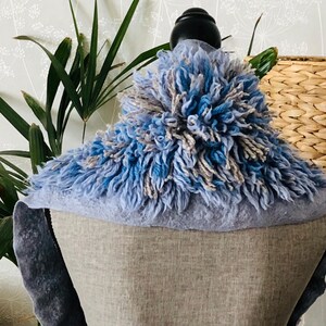 Pode incluir: Uma echarpe felpuda azul e cinza com um detalhe de pompom. A echarpe &eacute; exibida em um manequim.