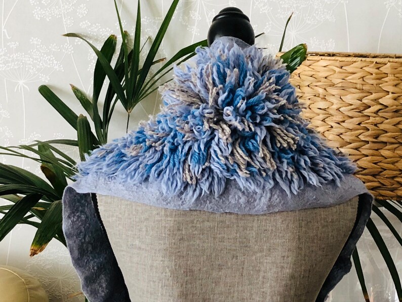 Pode incluir: Uma echarpe felpuda azul e cinza com um detalhe de pompom. A echarpe &eacute; exibida em um manequim.