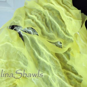 May include: A yellow silk shawl with a textured, wavy pattern. The shawl is draped over a dark surface and has the text "Galina Shawls" printed on it.