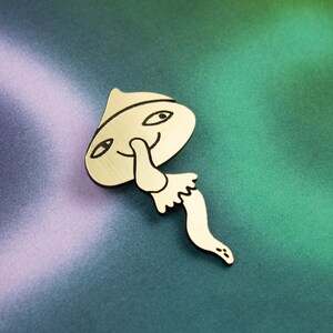 May include: A gold-coloured metal pin shaped like a mushroom with a smiling face and a long, thin stem. The mushroom is wearing a hat.