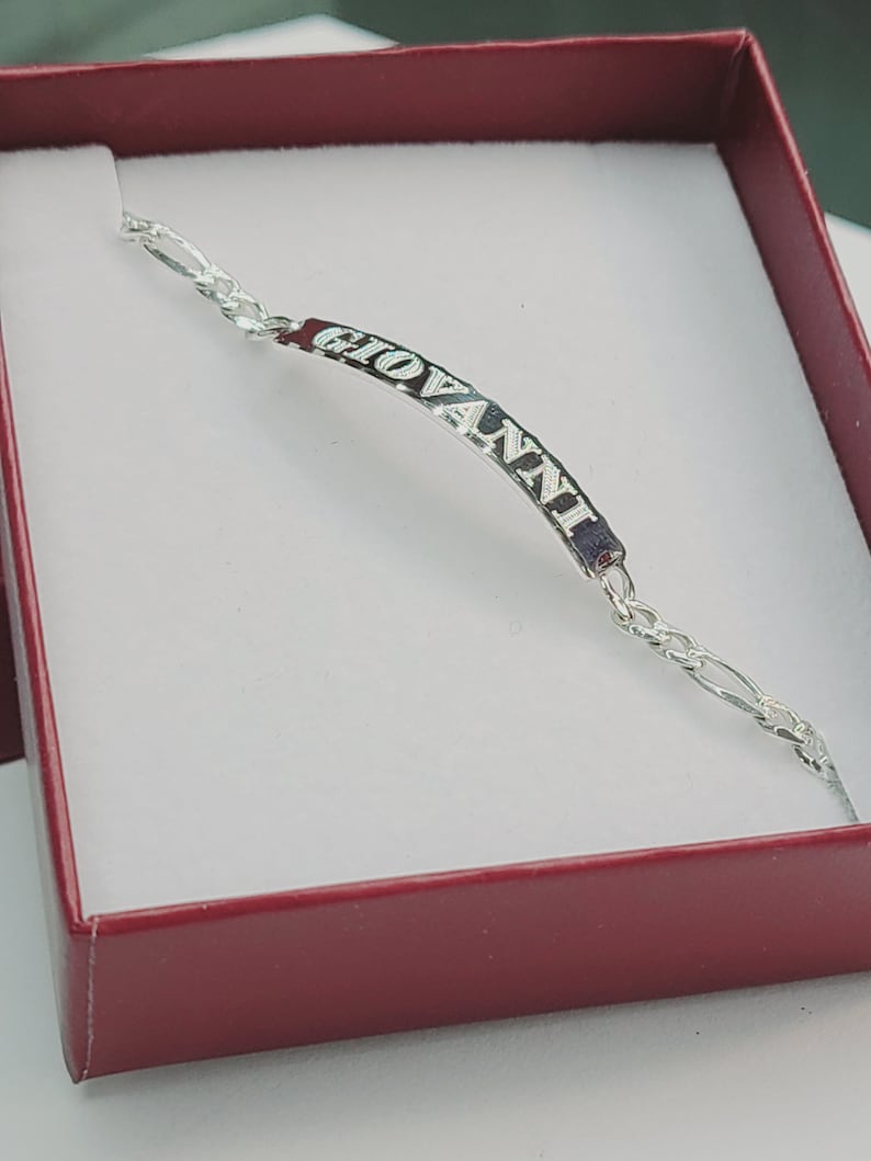 May include: A silver bracelet with a nameplate that reads "GIOVANNI". The bracelet is in a red box.
