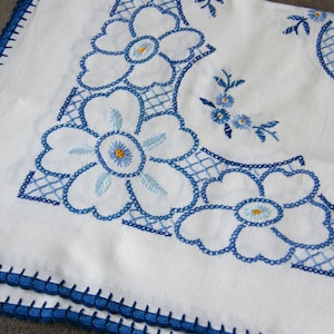 May include: White tablecloth with blue and yellow embroidered flowers. The tablecloth has a crocheted border.
