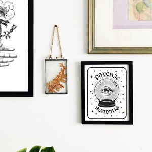 Puede incluir: Impresi&oacute;n de arte imprimible en blanco y negro con un marco negro. La impresi&oacute;n presenta una ilustraci&oacute;n estilizada de un ojo dentro de una bola de cristal con el texto "Psychic Reading" arriba y abajo de la imagen.