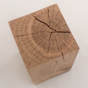Puede incluir: Un taburete cuadrado de madera con un acabado de madera natural. La parte superior del taburete es una sección transversal de un tronco de árbol, que muestra la veta y los anillos.