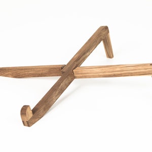 May include: A wooden laptop stand with a natural finish. The stand is made of two pieces of wood that are crossed at the center and have angled legs.