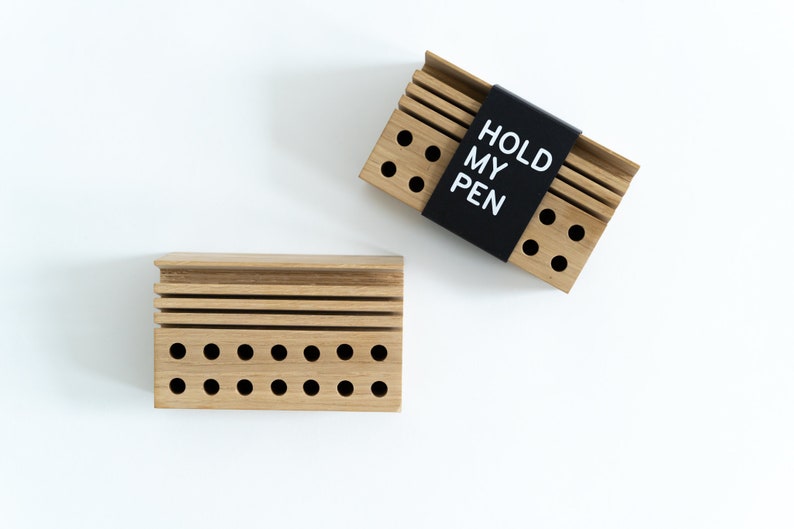 May include: Two wooden pen holders with a black label on one that says "HOLD MY PEN". Both holders have multiple holes for pens and pencils.