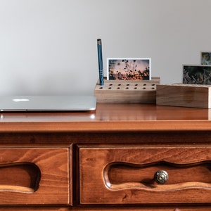 May include: A wooden desk organizer with a pen holder and slots for photos. The organizer is on a wooden desk with two drawers. A laptop is on the desk.