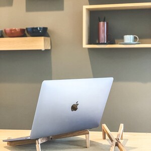May include: A silver laptop computer on a wooden stand with a second wooden stand next to it. The laptop is on a light wood surface.
