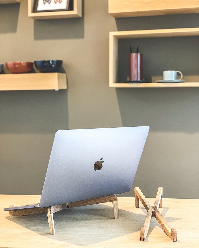 May include: A silver laptop computer on a wooden stand with a second wooden stand next to it. The laptop is on a light wood surface.