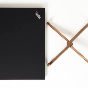 May include: A black laptop computer with the ThinkPad logo on the lid, next to a wooden laptop stand.