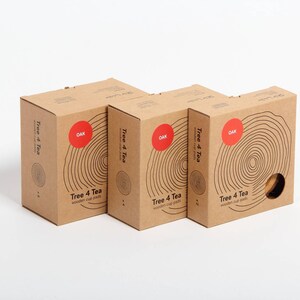 Puede incluir: Tres cajas de cart&oacute;n marr&oacute;n con el texto "Tree 4 Tea" y "OAK" impreso en ellas. Las cajas est&aacute;n apiladas una encima de la otra y tienen un patr&oacute;n de veta de madera.