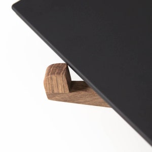 May include: A black rectangular serving tray with a wooden base. The tray is angled and the wooden base is visible. The base is made of dark wood with a natural grain.