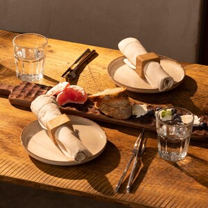 May include: A wooden serving tray with a light brown finish, featuring a napkin ring, a slice of grapefruit, a piece of bread, and a small bowl of blueberries. The tray is set on a wooden table with two glasses of water and a set of silverware.