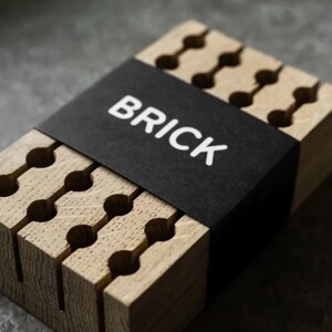 May include: A wooden organiser with a black label that says "BRICK". The organiser has multiple slots for storing items like pens, pencils, or other small objects.