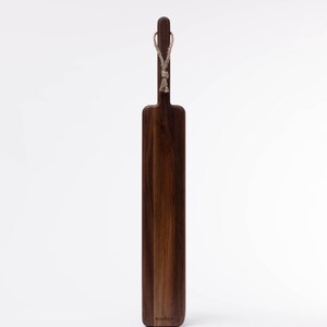 May include: A long, rectangular wooden cutting board with a dark brown finish. It has a rope handle and the word "woodlot" is engraved on the bottom.