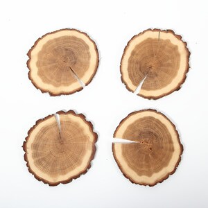 Puede incluir: Cuatro posavasos redondos de madera con veta de madera natural y color marr&oacute;n claro. Cada posavasos tiene una grieta en el centro.