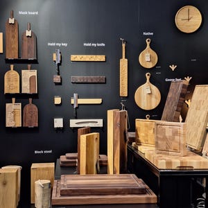 May include: A display of wooden cutting boards and serving trays, with various sizes and shapes. The boards are made in Lithuania and are labeled with names like "Native", "Hold my knife", and "Goose feet". The sign above reads "Hand Made in Lithuania" and "We Produce Private Label".