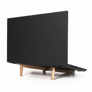 May include: A black laptop computer on a wooden stand. The laptop is closed and the Lenovo logo is visible on the back.