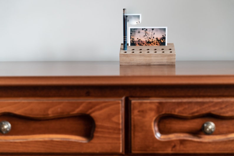 May include: A wooden photo holder with a natural finish and a grid of holes to hold photos. A photo of a field of flowers at sunset is displayed in the holder.