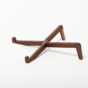 May include: A wooden laptop stand made of walnut wood. The stand is in the shape of an X and has a natural wood finish.