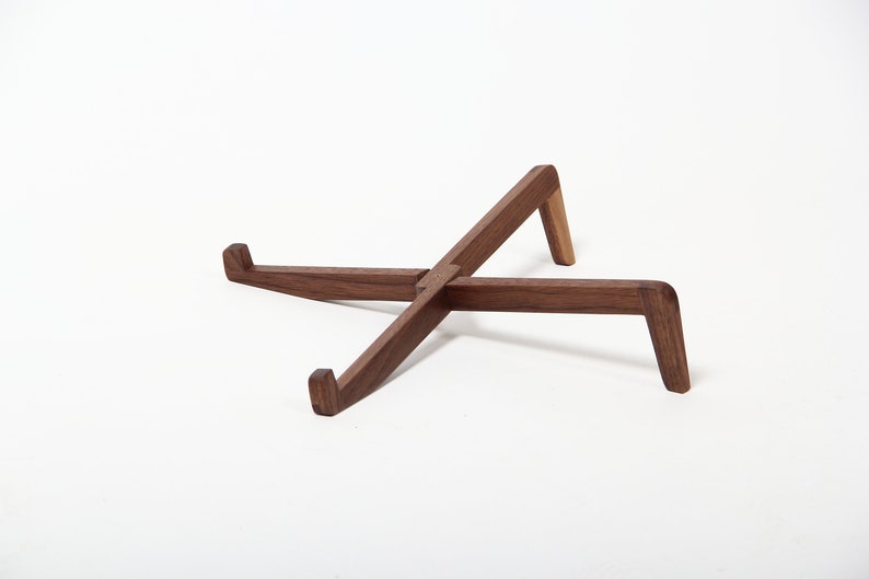 May include: A wooden laptop stand made of walnut wood. The stand is in the shape of an X and has a natural wood finish.