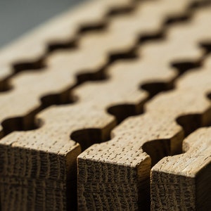 May include: Close-up of a wooden board with a repeating pattern of interlocking grooves. The board is light brown in colour and has a natural wood grain.