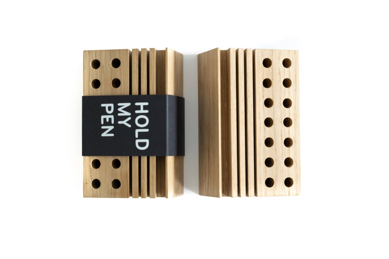 May include: Two wooden pen holders with a black label that reads "HOLD MY PEN". Each holder has multiple rows of holes for pens.
