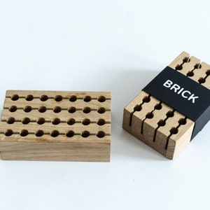 May include: Two wooden pencil holders, one with a grid of holes and the other with vertical slots. The holder with slots has a black label that says "BRICK".