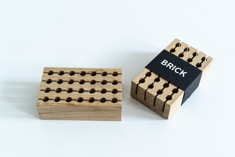May include: Two wooden pencil holders, one with a grid of holes and the other with vertical slots. The holder with slots has a black label that says "BRICK".