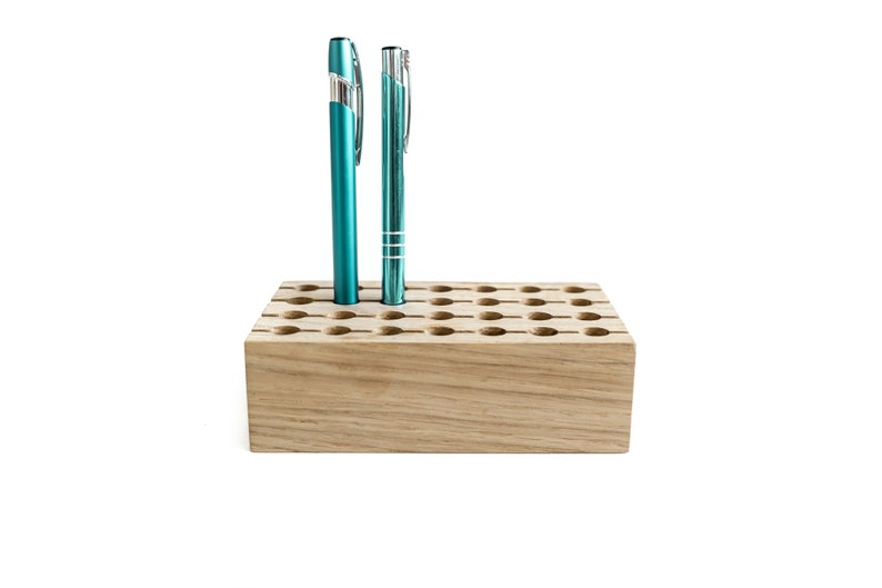 May include: A wooden pen holder with 36 holes, featuring two teal pens inserted. The holder is made of light brown wood with a natural grain.