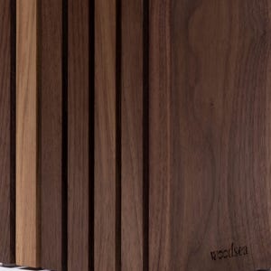 May include: A vertical wooden knife block constructed from multiple dark brown walnut slats with one lighter tan slat integrated into the design. The block features a smooth finish and the word woodsea is embossed on the lower right side.
