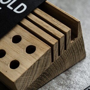 May include: A wooden organizer with slots for holding knives and a section with three round holes. The organizer is made of light brown wood and has a natural finish. The text "HOLD MY KNIVES" is printed on a black label attached to the organizer.