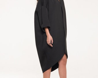 May include: A black, long-sleeved, asymmetrical dress with a high neckline. The dress is made of a thick, textured fabric. The model is wearing black platform heels.
