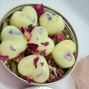 May include: A tin container filled with heart-shaped white wax melts, scattered with dried rose petals. The container is on a white surface.