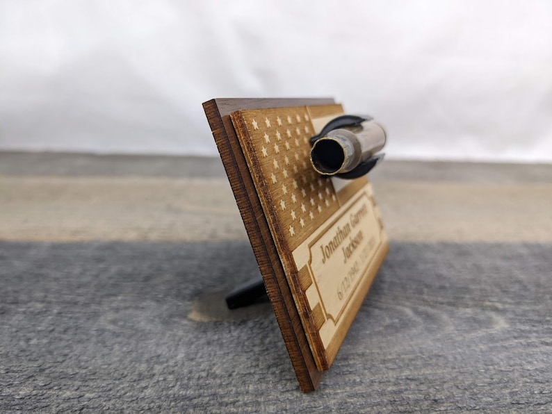A wooden plaque with a US flag design and a brass shell casing mounted on top.