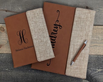 May include: Two brown leather and beige fabric personalized folders with a pen. The smaller folder has the monogram "H" and the name "Melanie Hackman". The larger folder has the name "Audrey" in cursive.