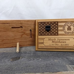 May include: A wooden plaque with an American flag and the Air Force seal. The plaque is engraved with the name "Mark Jameson Matthews" and the dates "11/30/1953 - 8/1/2021".