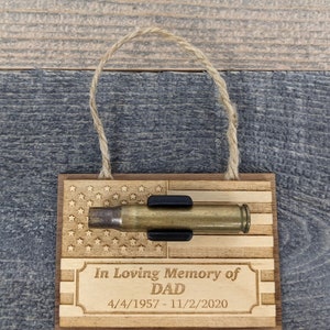 May include: Wooden ornament with an American flag design, a bullet casing, and the text "In Loving Memory of DAD 4/4/1957 - 11/2/2020".