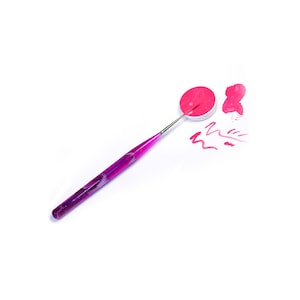 May include: A purple and silver nail art tool with a pink nail polish pot and a pink smear on a white surface.