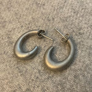 May include: A pair of silver hoop earrings with a smooth, rounded finish. The earrings are simple and elegant.