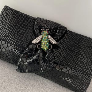 May include: Black snakeskin clutch with a jeweled bee brooch. The bee is green, black, and clear with rhinestones.