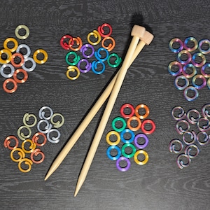 May include: A set of colorful plastic rings, a rainbow of colors, and two wooden knitting needles. The rings are arranged in a circle pattern, with the needles in the center.