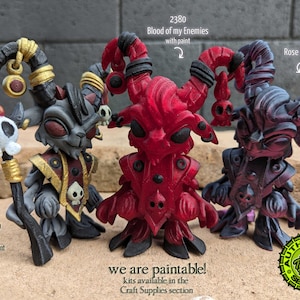 Könnte beinhalten: Drei kleine, detaillierte, 3D-gedruckte Figuren von gehörnten Kreaturen. Die Figuren sind in Grau, Rot und einer Kombination aus Rosarot und Schwarz bemalt. Der Text "we are paintable!" ist unter den Figuren sichtbar.