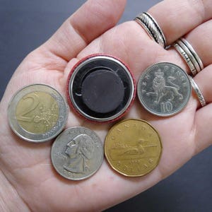 Pu&ograve; includere: Una collezione di monete di diversi paesi, tra cui una moneta canadese da un dollaro con un loon, una moneta da 2 euro, una moneta da 10 pence con un leone e un bottone rosso e argento.
