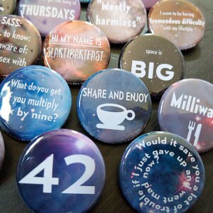 Pu&ograve; includere: Una collezione di bottoni rotondi colorati con varie frasi e disegni. I bottoni presentano uno sfondo simile a una galassia con testo bianco. Alcune delle frasi includono "Thursdays", "Mostly harmless", "Space is BIG", "Share and Enjoy", "What do you get if you multiply by nine?", "42", e "Milliways".