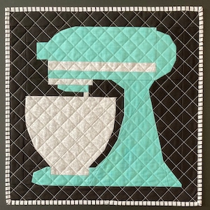 May include: A teal blue stand mixer with a white bowl. The mixer is quilted and has a black background.